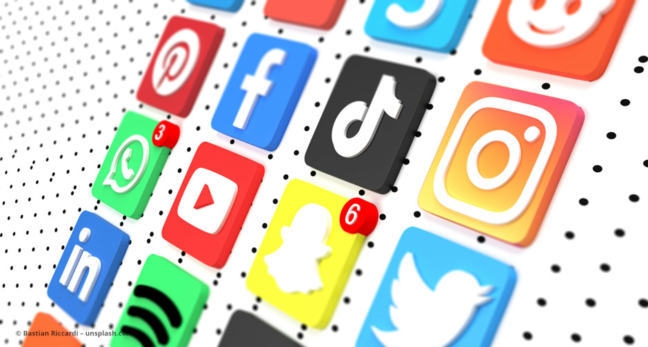Viele bunte Social Media Icons auf einem weißen Untergrund mit kleinen schwarzen Löchern © Bastian Riccardi – unsplash.com