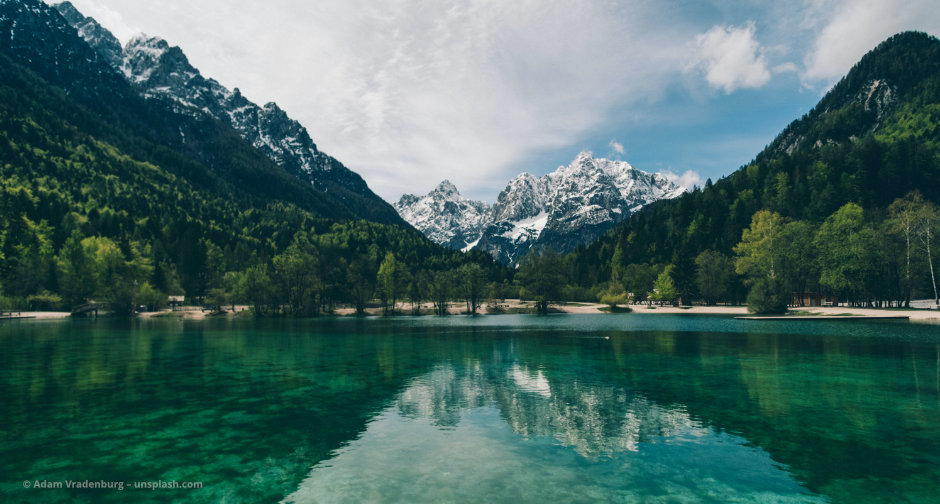 Teils schneebedeckte Berge am Horizont spiegeln sich im See © Adam Vradenburg – unsplash.com